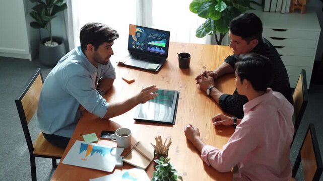 Executive manager explain financial graph to colleague at meeting room. Top aerial view of diverse marketing team sharing idea and planning strategy while sitting at table with tablet. Convocation.