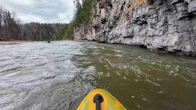 Kayak hugging towering limestone cliff edge, paddler threading fast current beside sheer rock face, splashing water and textured strata, adrenaline and technical balance required