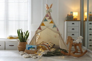 Cute wigwam with fairy lights and toys in stylish child's room © New Africa