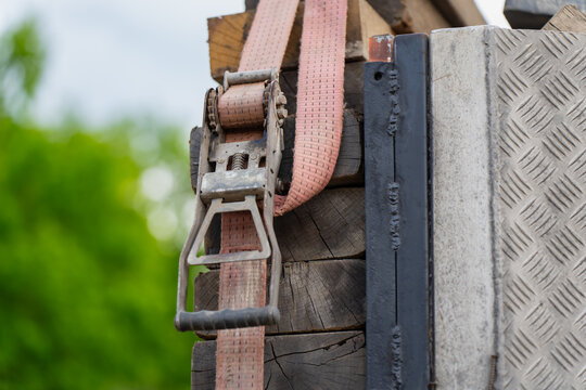 Industrial ratchet tie down strap securing stacked wooden beams on a construction vehicle trailer bed, heavy cargo transport logistics and load safety