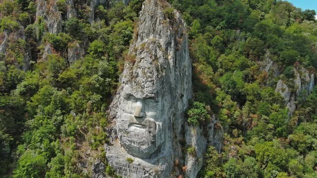 Aerial around view of stone carved statue portrait of ancient dacian king Decebal. Sculpture located on shore of Danube River, Romania, 4k