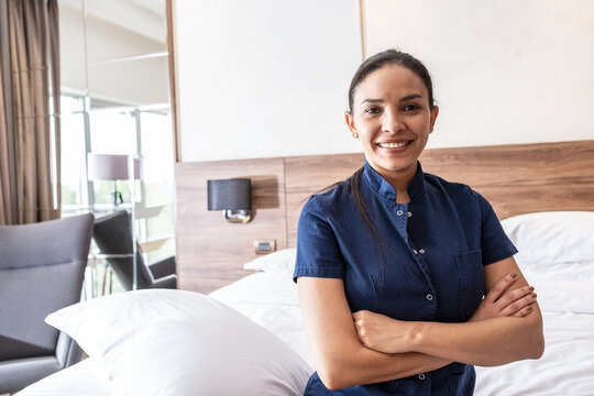 A female hotel staff member is preparing a room for the next guests. She carefully makes the bed, arranges pillows, and ensures the room is tidy and ready for service.