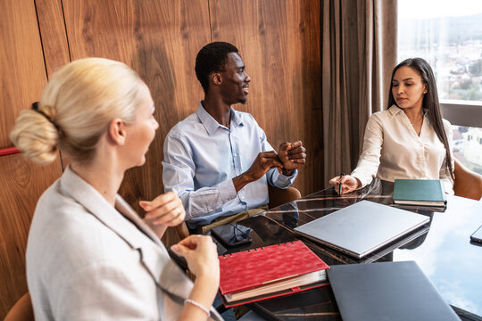 A group of young business people are sitting together in the office, brainstorming ideas and discussing future projects, while taking notes and sharing suggestions.
