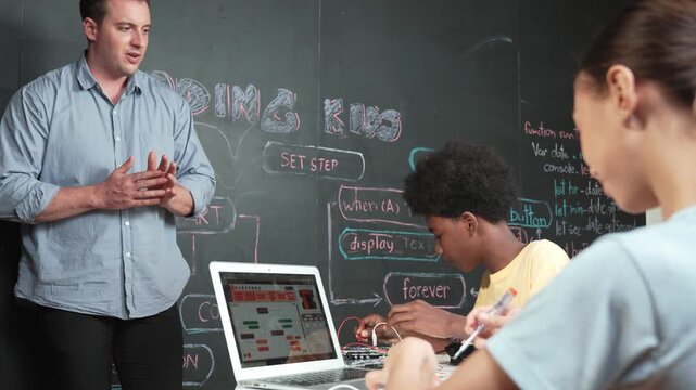 Teacher teaching about coding system while diverse academic student fixing main board at table with laptop display programming prompt or engineering code at STEM technology classroom. Edification