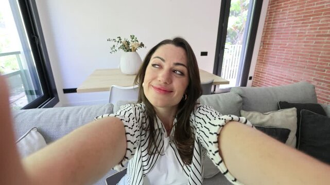 Pov shot of a beautiful young woman vlogging at home from her couch, smiling and making silly faces while talking directly to the camera for her followers and sharing content on social media