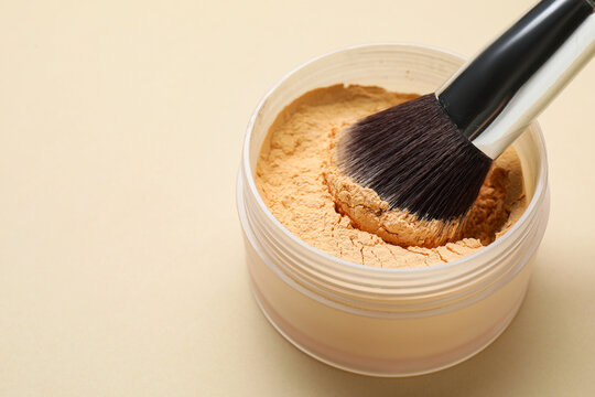 Loose face powder and brush on beige background, closeup. Space for text