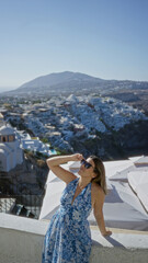 Obraz premium Woman raising arm with sunglasses on a white building terrace, leaning on a wall and smiling at the view; vacation serenity.
