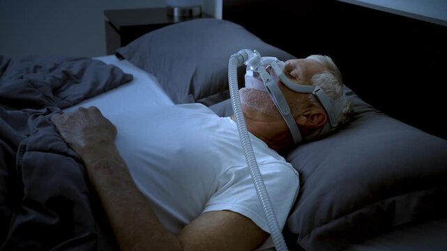 Mature adult sleeping at night while wearing a CPAP mask to treat his Sleep Apnea.