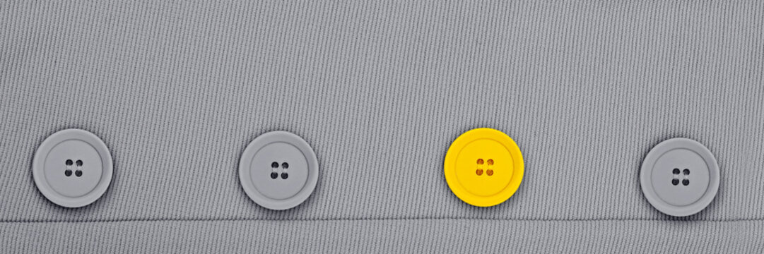 Four buttons on a gray fabric with one yellow button standing out among the gray ones