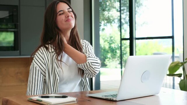Young female freelancer working on a laptop at her home office suffering from neck and shoulder pain caused by poor posture, a sedentary lifestyle, and overworking at her desk