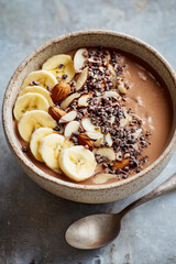 Fototapeta premium Healthy chocolate smoothie bowl topped with fresh sliced bananas, almonds, and cacao nibs in a ceramic bowl. Perfect delicious and nutritious breakfast
