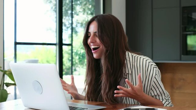 Overjoyed successful woman reading an email with amazing news on her laptop, celebrating a victory or achievement with ecstatic gestures and a happy dance while working from her modern home