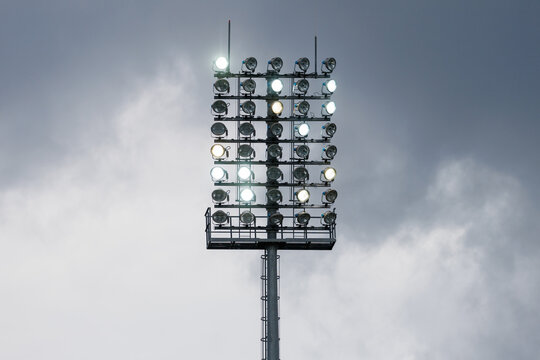 Sport stadium light mast with glowing spotlights on a rainy day