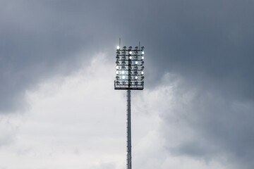 Obraz premium Sport stadium light mast with glowing spotlights on a rainy day