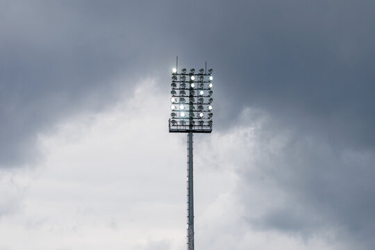 Sport stadium light mast with glowing spotlights on a rainy day