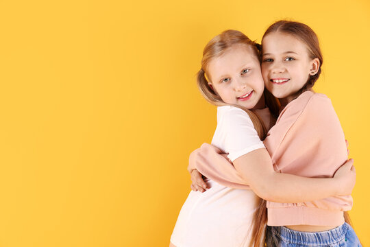 Cute little sisters hugging on yellow background, space for text