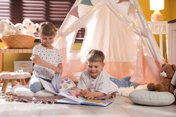 Little girl and boy reading books near wigwam at home © New Africa