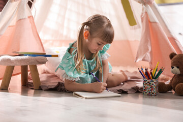 Little girl drawing near wigwam at home © New Africa