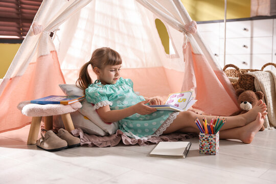 Little girl reading book in wigwam indoors