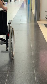 A faceless woman pushes a wheelchair through a shopping mall.