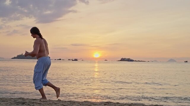 Shirtless man running along a beach at sunset. A shirtless adult man runs along a sandy beach at sunset, with calm water, distant islands, and a warm golden sky creating a peaceful coastal scene