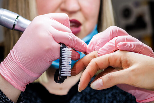 Manicurist performing nail care procedure using brush and electric file in a salon