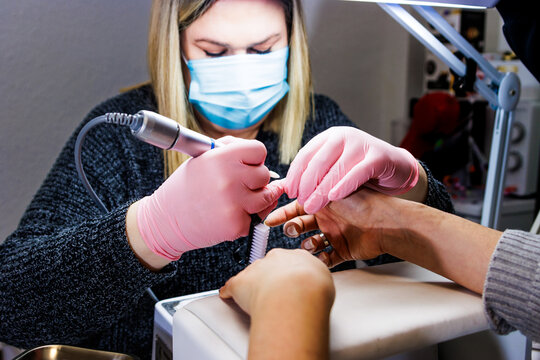 Professional manicurist working on client nails using an electric nail file