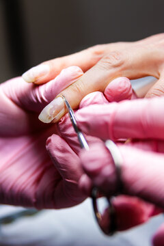 Manicurist removing cuticles from client's finger with scissors in beauty salon