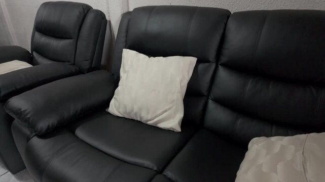 Sof&aacute; reclinable de cuero negro con cojines blancos en sala de estar moderna, mueble de hogar contempor&aacute;neo