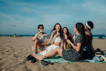 Obraz premium Diverse friends enjoying summer picnic on beach, drinking beverages and celebrating togetherness
