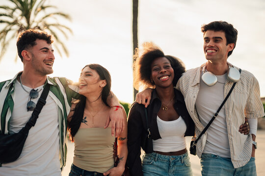 Diverse young friends walking together, embracing happiness and unity during sunset outdoors