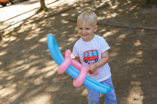 Smiling little boy playing with twisted balloon toy in shaded park
