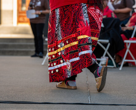 Close-up of a person wearing a traditional red ribbon skirt with MMIP (Missing and Murdered Indigenous Peoples) red handprint motifs. 