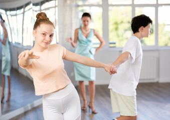 Fototapeta premium Smiling teenage girl practicing vigorous jitterbug moves with partner during dance lesson in choreography studio