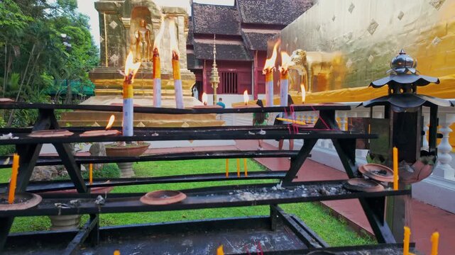 Burning candles and incense sticks at a Buddhist temple in Chiang Mai, Thailand, symbolize devotion and prayer. Visitors offer these items for spiritual reflection.