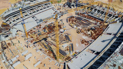 Fototapeta premium Large stadium building site showing concrete structures, many yellow cranes, and construction materials on the ground, representing urban development and infrastructure growth
