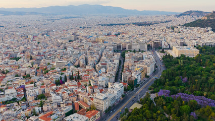 Obraz premium Athens urban landscape featuring the hellenic parliament building next to the lush national garden and a bustling avenue, extending towards distant mountains under a clear sky