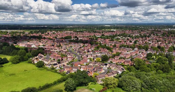 Aerial drone footage of the town of Acomb in York North Yorkshire UK showing residential housing estates bordered by farmland grassland and mature woodland beneath a dramatic cloud filled sky