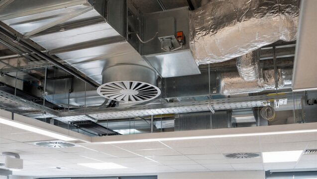 Modern hvac ventilation system with metal ductwork and circular air diffuser installed on building ceiling. Industrial climate control engineering for commercial office interior.