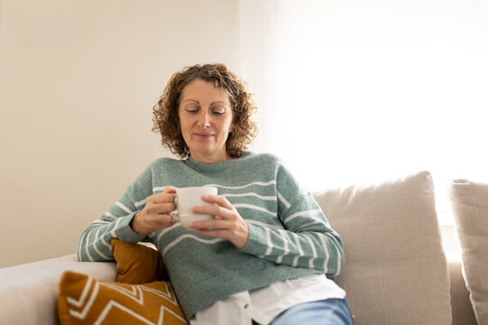 Woman relaxing at home, enjoying warm beverage in mug