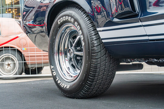 Close-up view of a classic American muscle car, possibly a Ford Mustang Shiny chrome hubcap with Ford embossed, black tire with visible treads and sidewall text reading - Kyiv, Ukraine 10-12-2024
