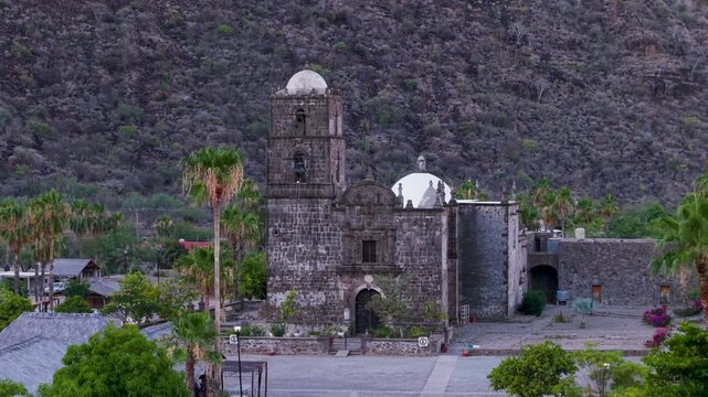 Discover the San Javier Mission in Baja California Sur with morning light illuminating the palm trees and the nearby town of Loreto