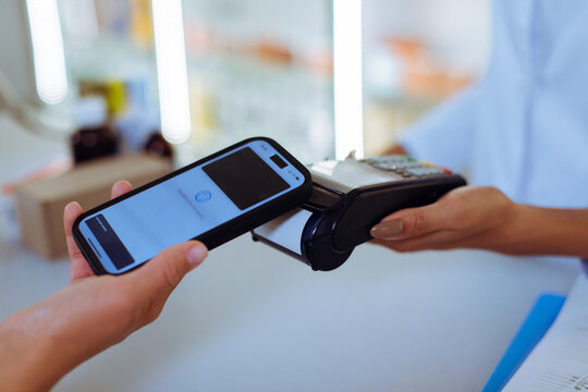 Customer making contactless NFC payment using smartphone at pharmacy POS terminal