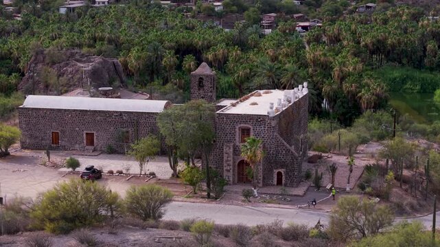 Aerial views reveal the Mission of Santa Rosalia amidst mountains, desert, and palm trees in Baja California Surs late afternoon.