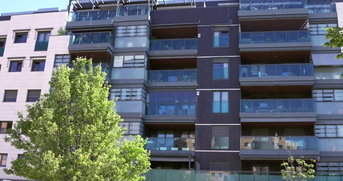 Contemporary residential apartment building with glass-fronted balconies and modern facade in Madrid, Spain. Urban housing architecture with large windows and residential living spaces under bright da