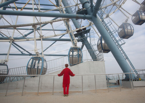A woman in the red outfit in the front of the ferris wheel 