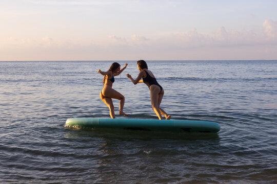 female friends jump to water from SUP, summer fun on beach, friendship