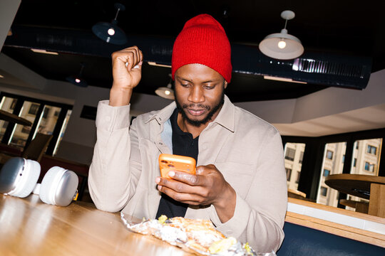 Young man wearing red beanie checking smartphone in cafe
