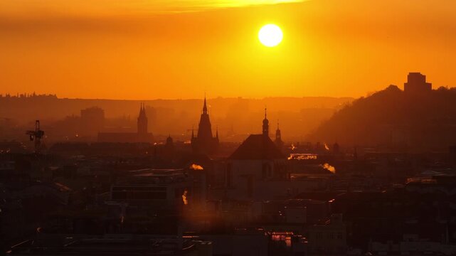 Aerial drone view of Prague historic city rooftops and church spires bathed in warm golden sunrise light with sun high in the orange sky, Prague, Czech Republic.