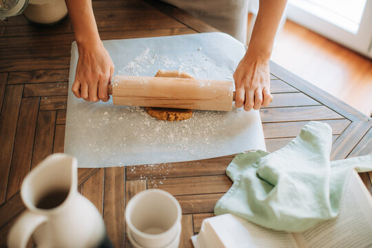 Top view of rolling dough with wooden rolling pin on table